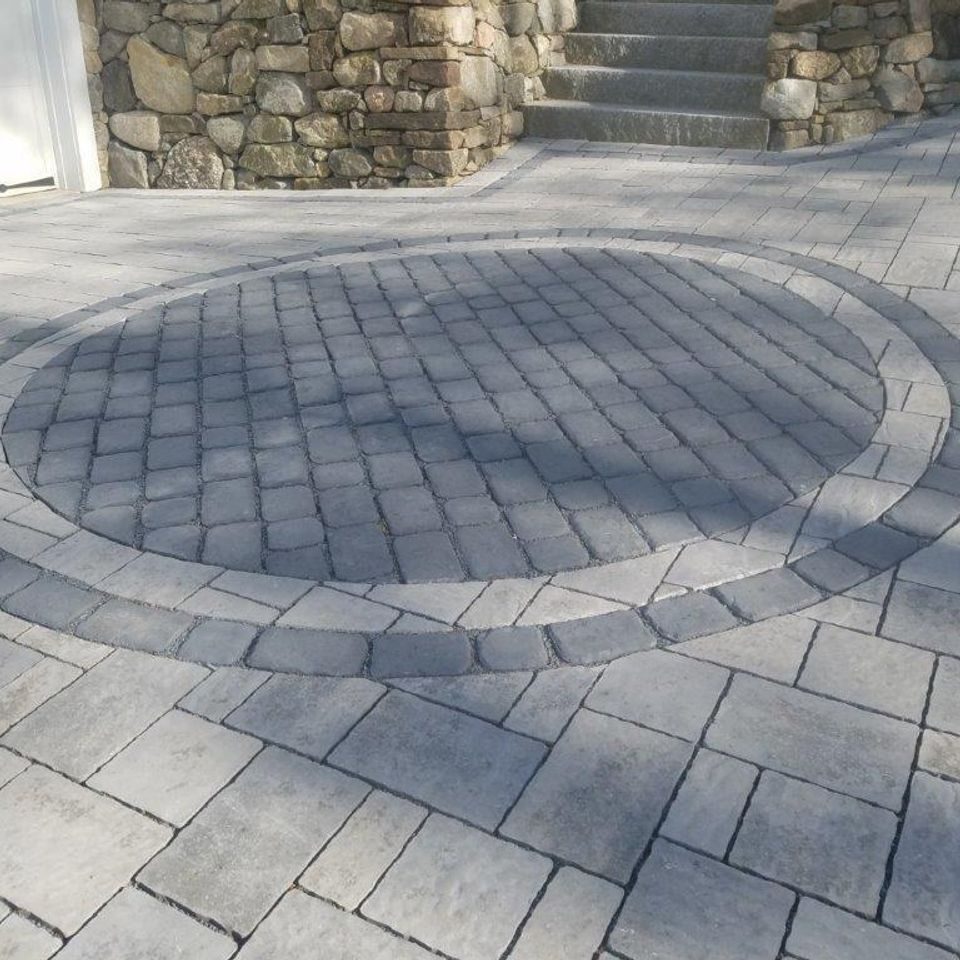Circular cobble inlay ringed by a border course, set into a grey paver driveway