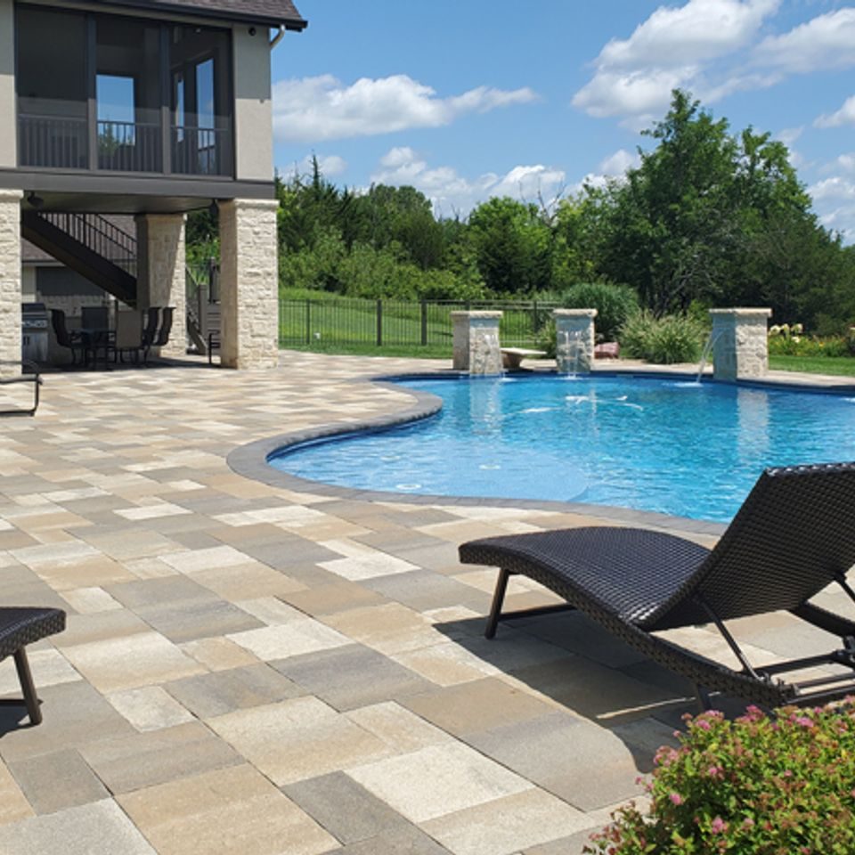 Paver pool deck curving around a freeform pool fed by stone scupper columns