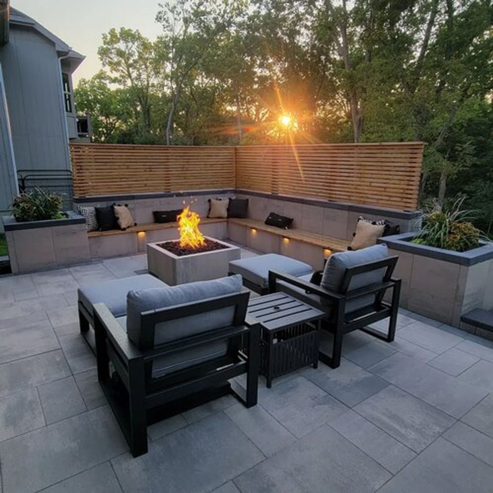 Modern slab patio with a square fire table, built-in bench and horizontal cedar screen at sunset