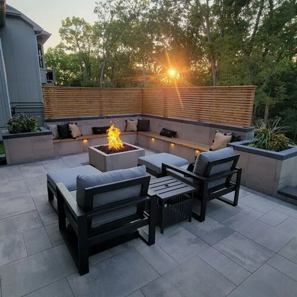 Modern slab patio with a square fire table, built-in bench and horizontal cedar screen at sunset