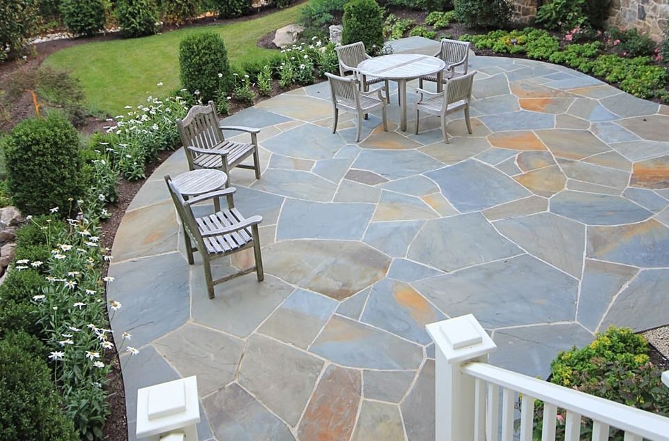 Circular bluestone flagstone patio with teak dining furniture beside a planted border