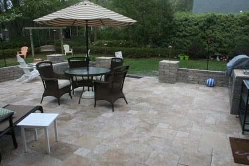 Travertine patio with block pillars, a seat wall and an umbrella dining set