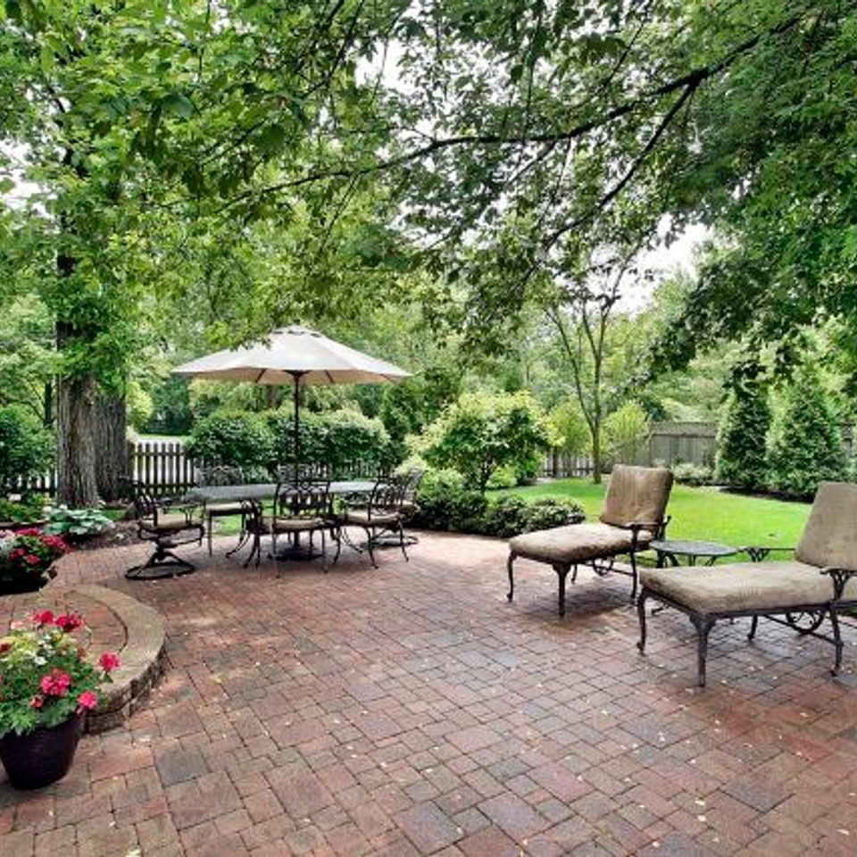 Clay brick patio with umbrella dining and lounge chairs under mature trees