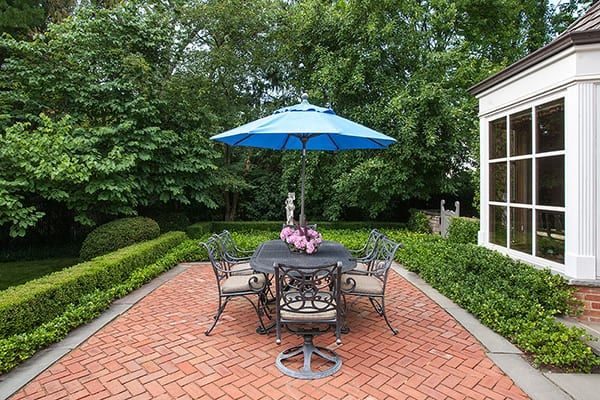 Red brick herringbone patio framed by boxwood, with a blue umbrella over the table