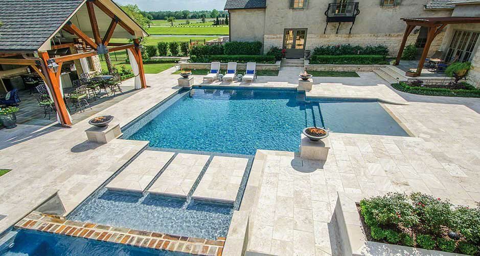 Ivory travertine pool deck framing a geometric pool with a raised spillway spa