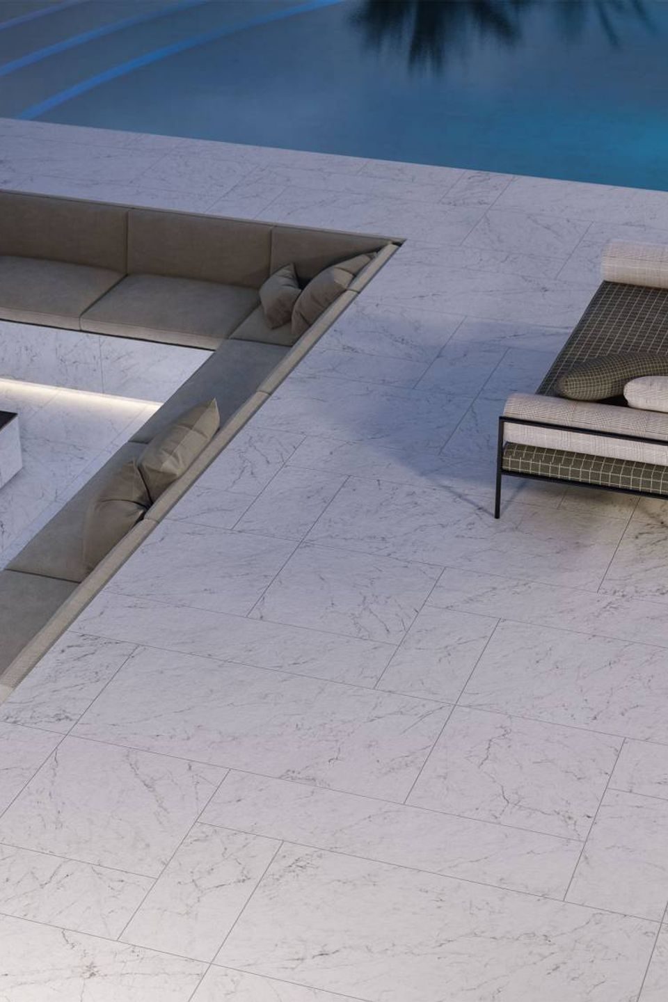 Sunken seating well set into a white marble-look pool deck beside a lit pool