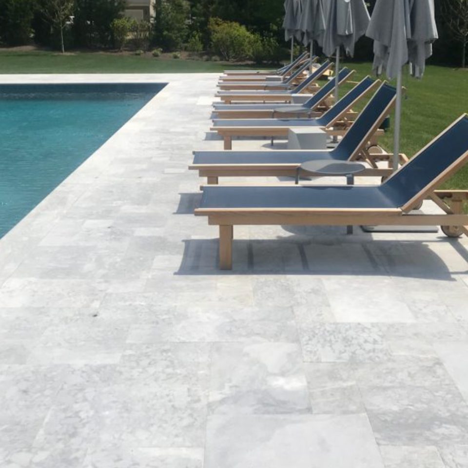 Row of teak loungers along a silver marble pool deck