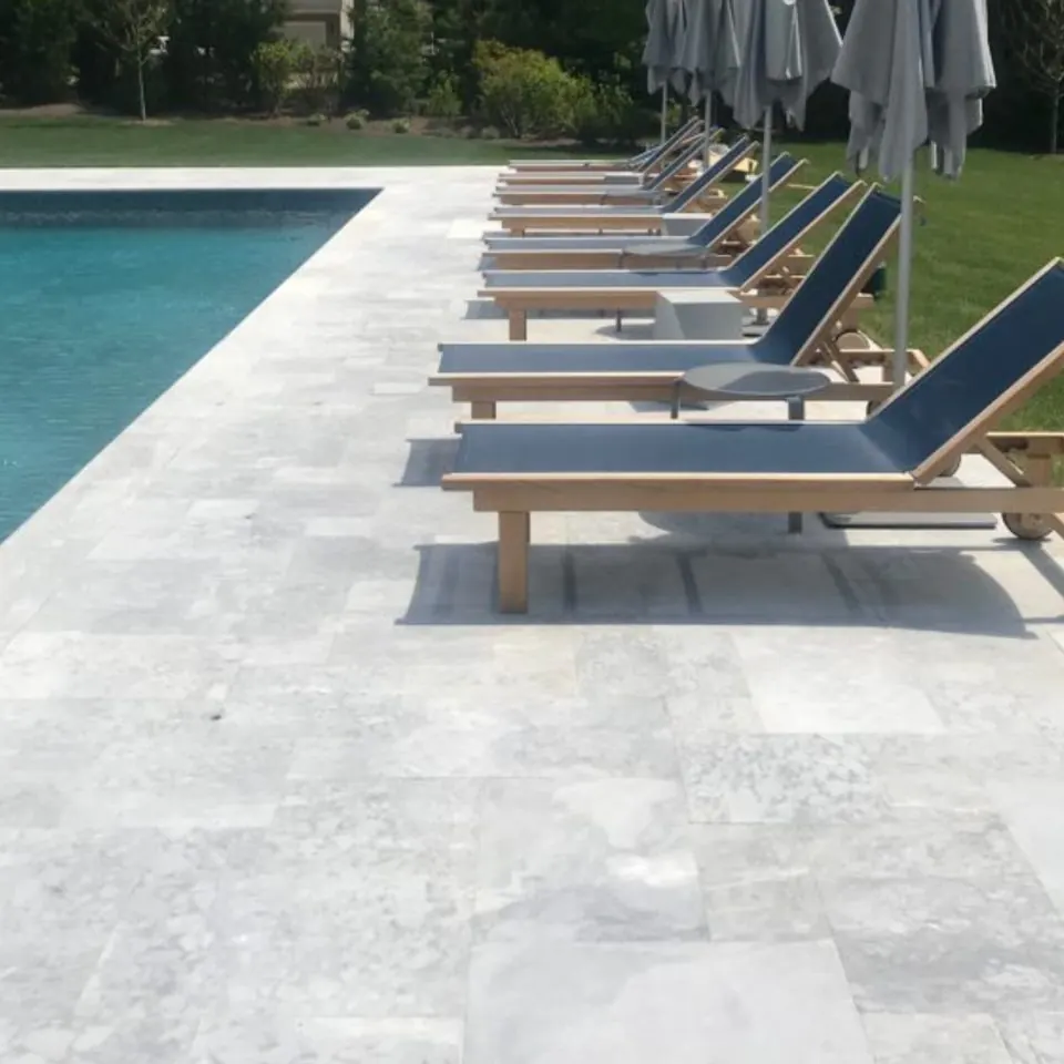 Row of teak loungers along a silver marble pool deck
