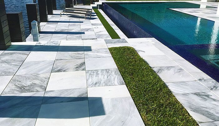 Marble paving and inset turf strips running alongside a dark-tiled pool