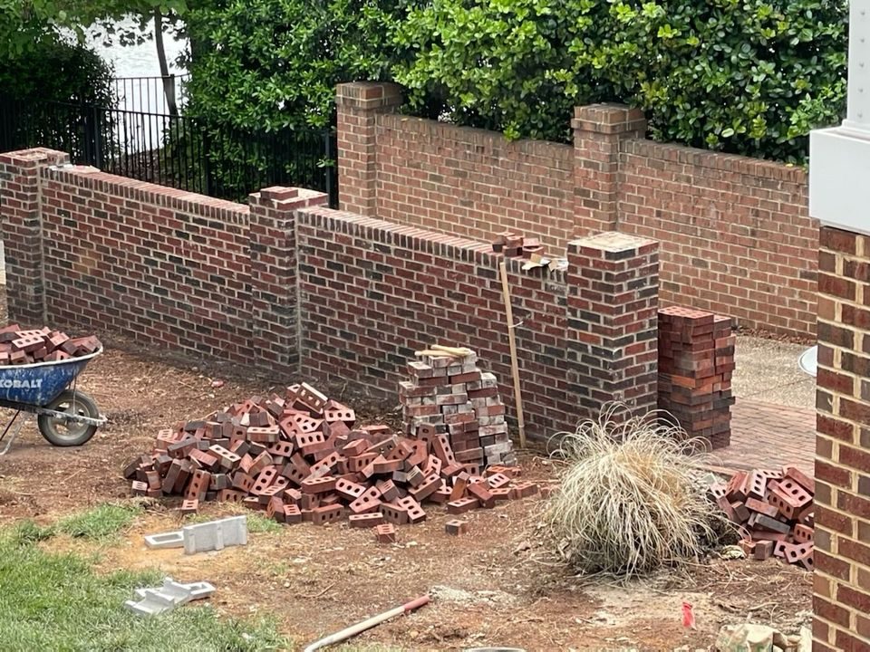 Brick boundary wall part-built, with bricks stacked and a wheelbarrow alongside