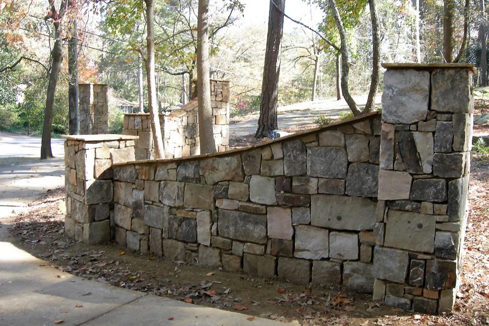 Dry-stacked stone wall with square capped columns running along a wooded drive