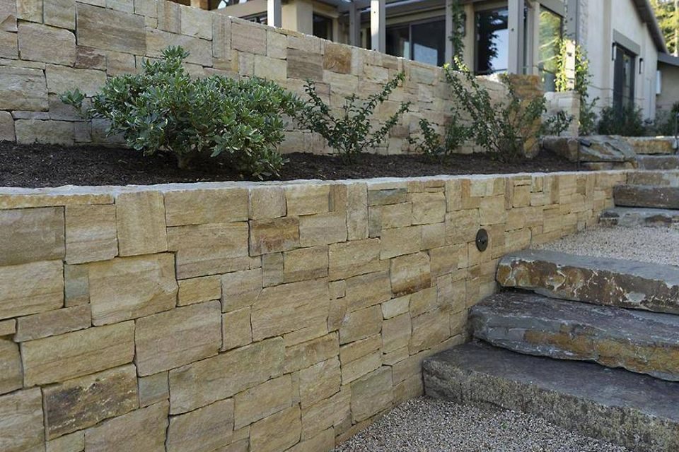 Terraced dry-stacked stone walls with a planted bed between and stone treads to one side