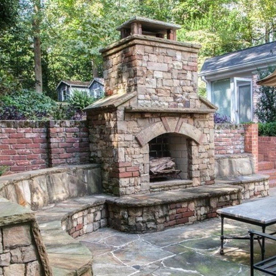 Stone and brick outdoor fireplace with a tall chimney and a curved hearth bench on a flagstone patio