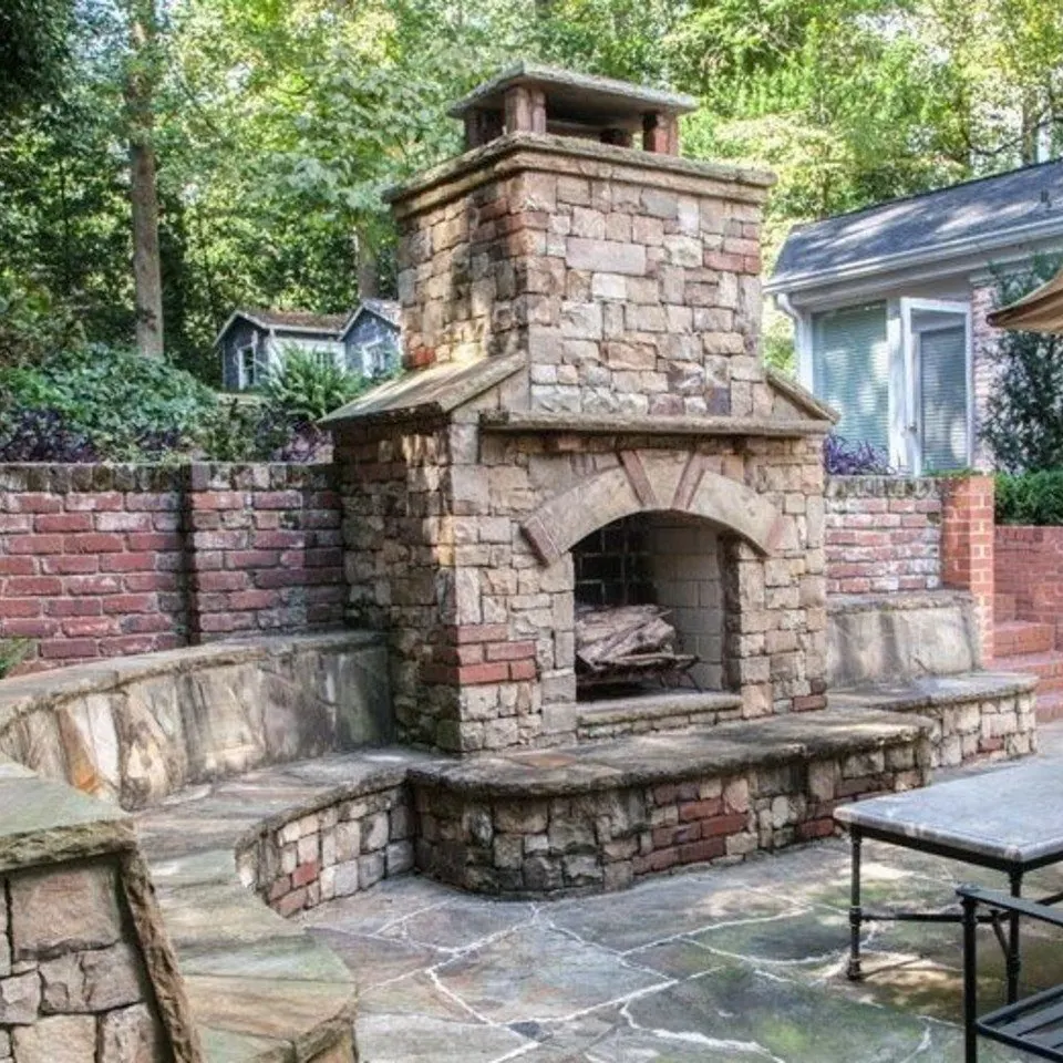 Stone and brick outdoor fireplace with a tall chimney and a curved hearth bench on a flagstone patio