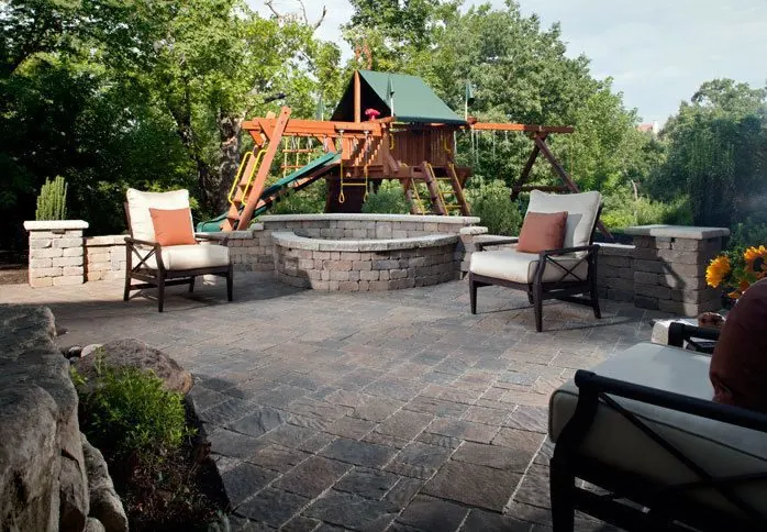 Block fire pit and seat wall on a paver patio, with a children's play set beyond