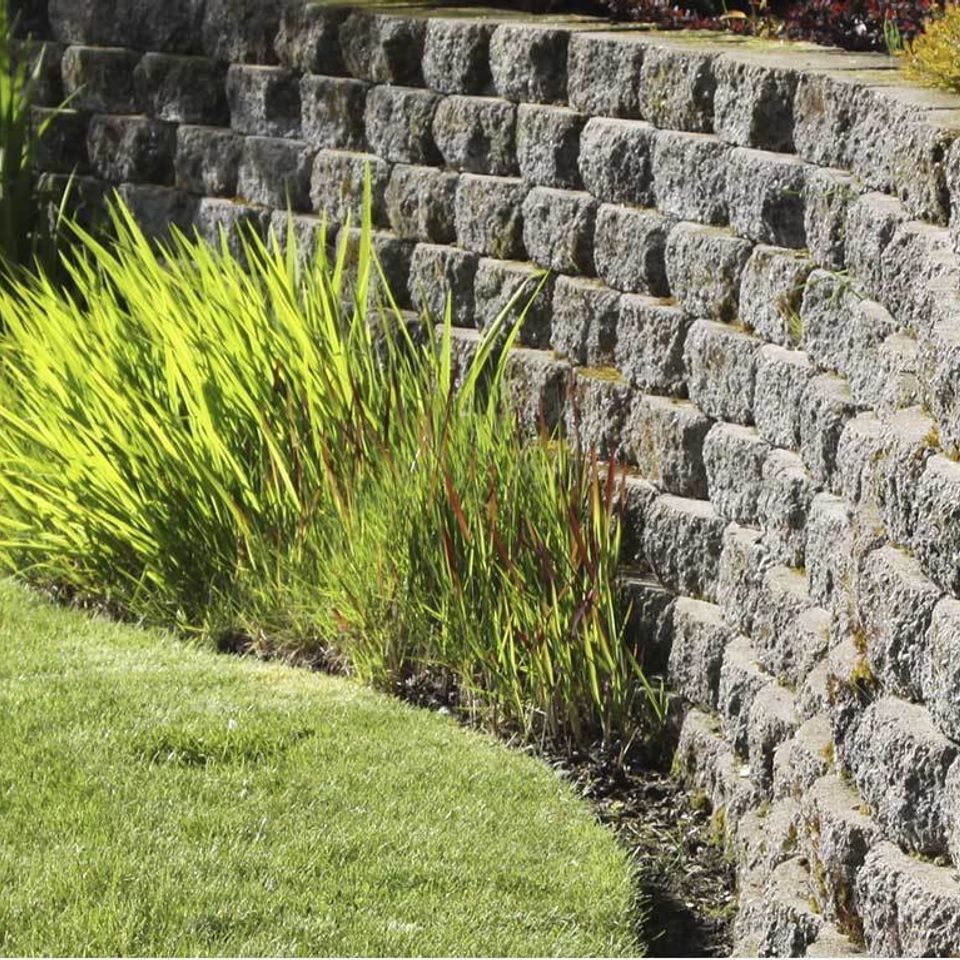 Split-face block wall curving along a lawn edge with ornamental grasses above