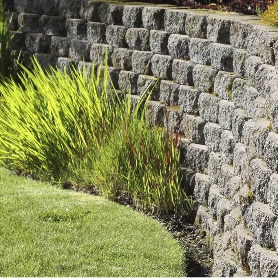 Split-face block wall curving along a lawn edge with ornamental grasses above