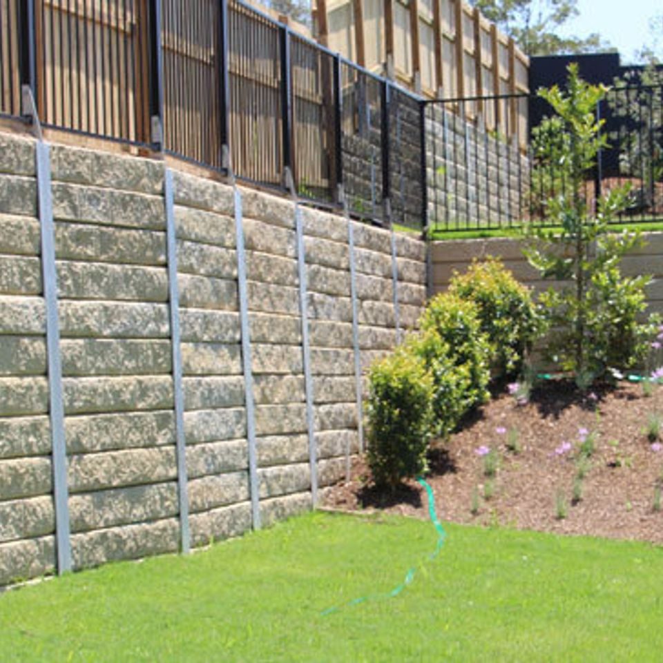 Post-and-panel concrete retaining wall holding a planted bank below a boundary fence