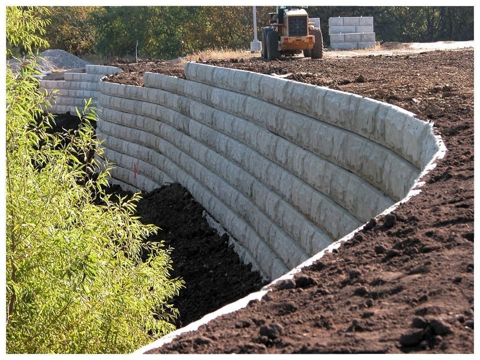 Curved segmental block wall part-built on an open site, with backfill and plant behind