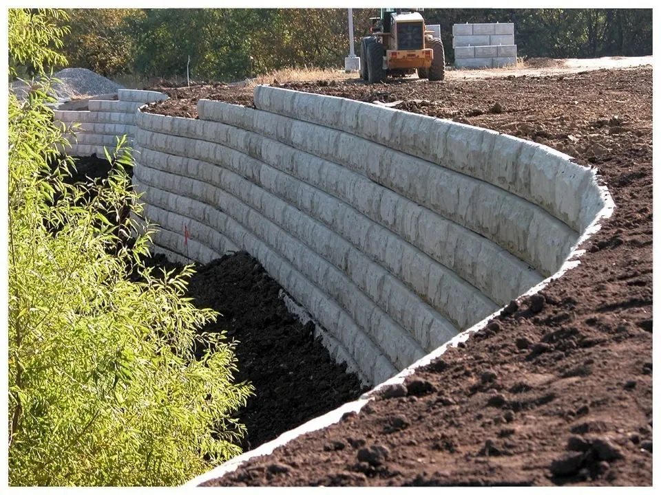 Curved segmental block wall part-built on an open site, with backfill and plant behind