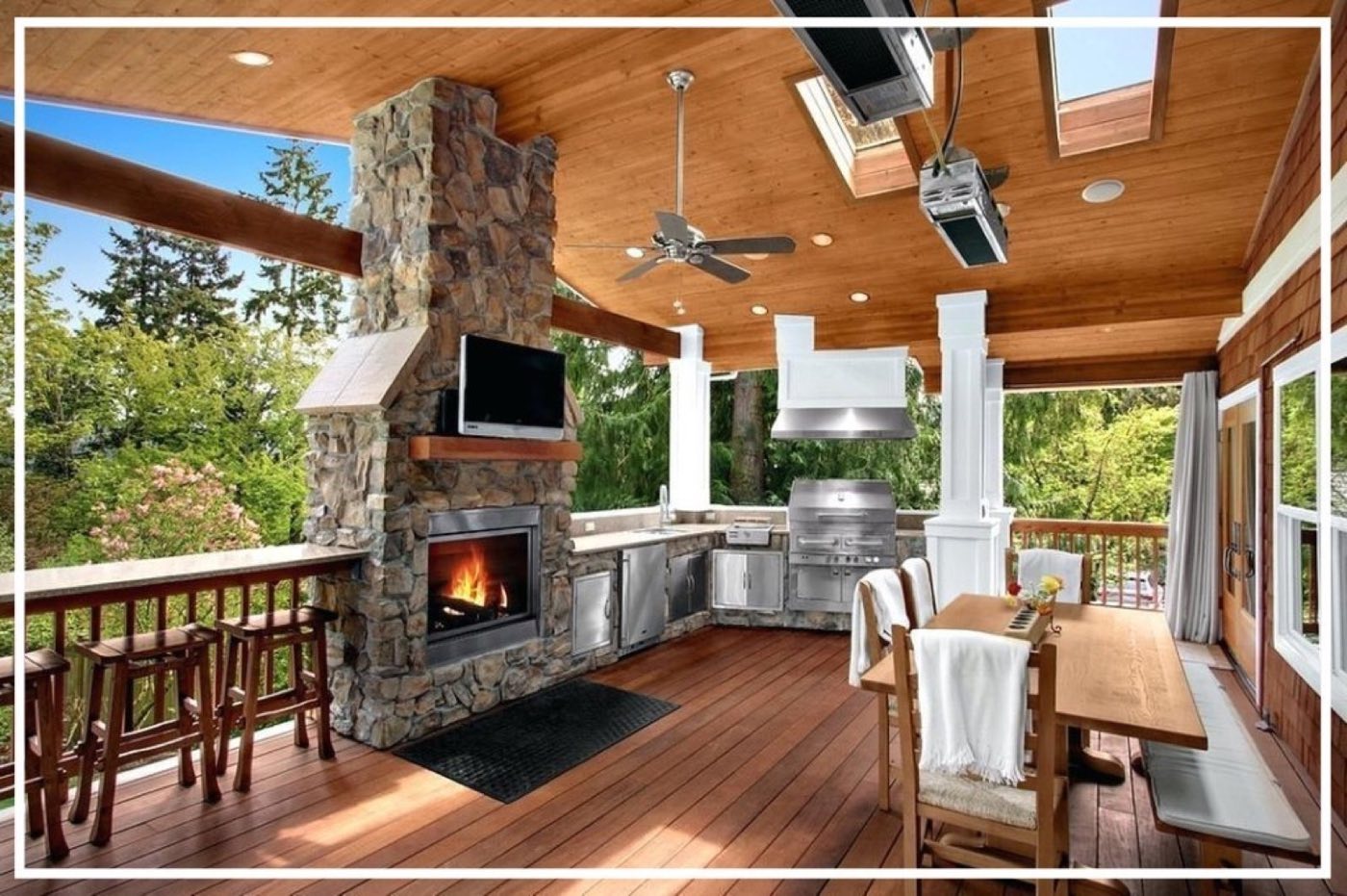Covered outdoor living room with a stone fireplace, mounted TV and a stainless grill run under a wood plank ceiling