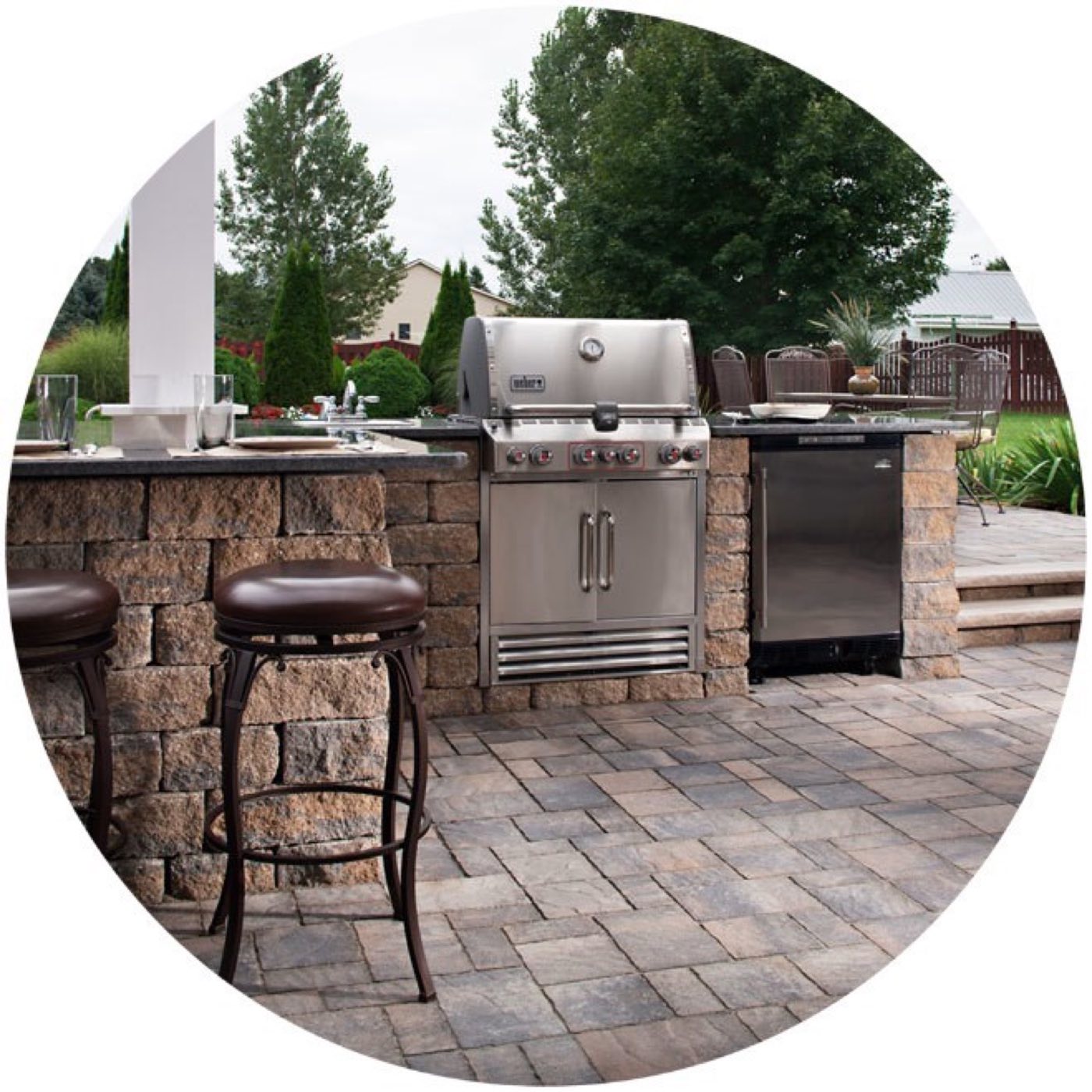 Stone-faced outdoor kitchen island with a built-in grill, beverage fridge and bar seating on a tumbled paver patio