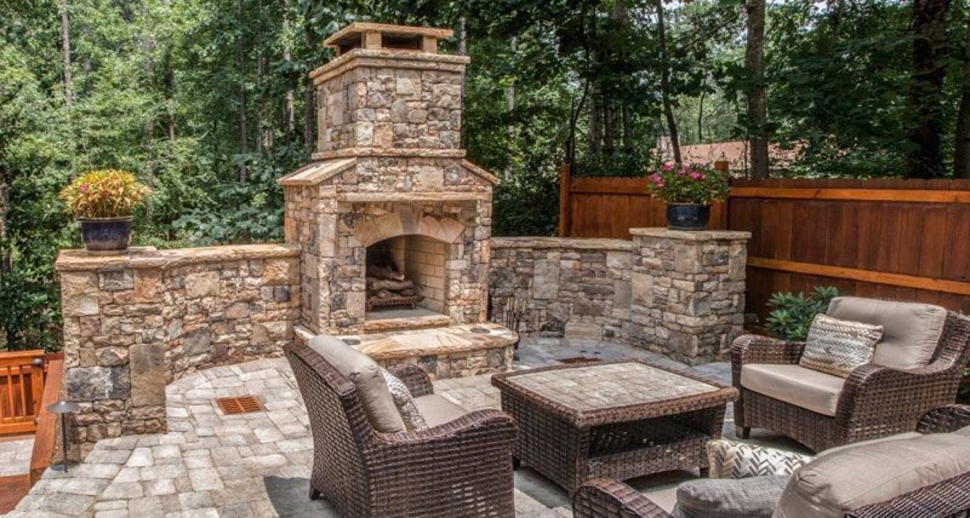 Stacked stone outdoor fireplace flanked by seat walls, with wicker seating on a paver patio