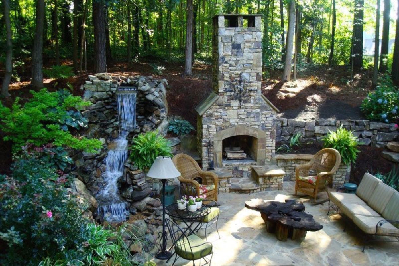 Wooded flagstone patio with a stone fireplace on one side and a rock waterfall on the other