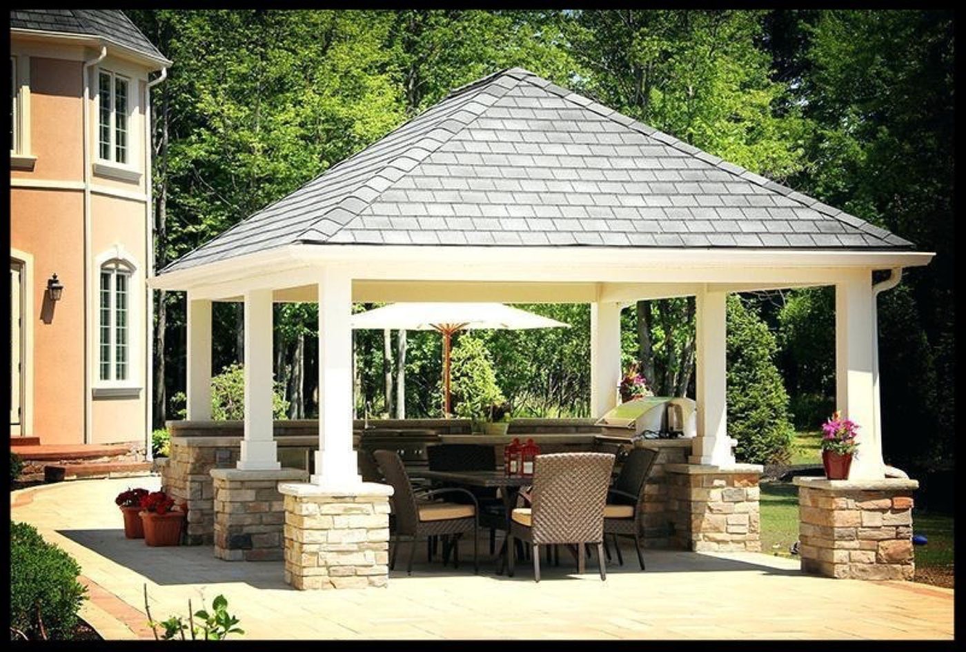 Hip-roof pavilion on stone-based columns sheltering an outdoor kitchen and dining table