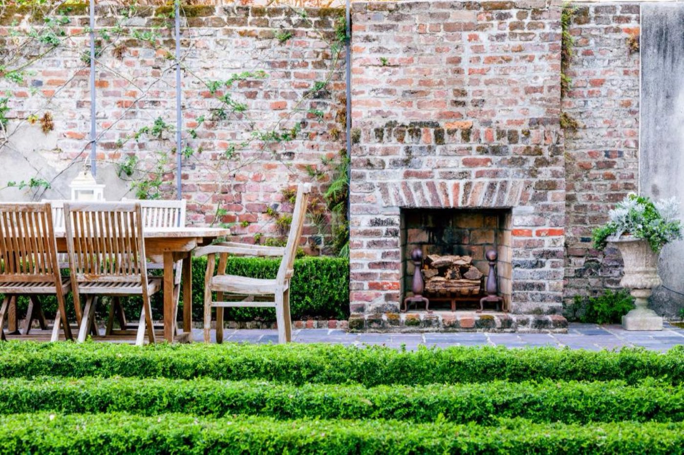 Brick garden wall with a built-in fireplace and iron fire grate behind a clipped boxwood hedge
