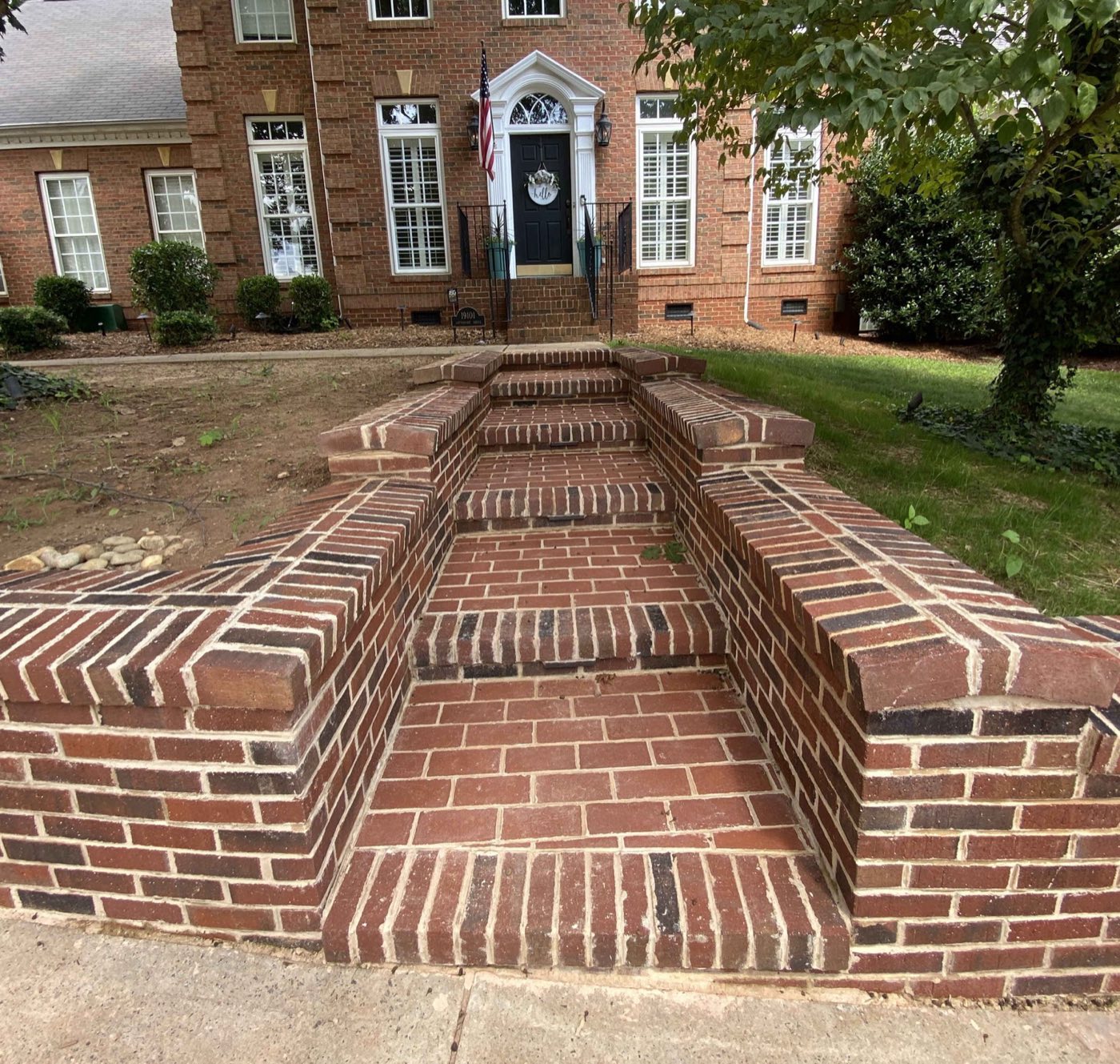Brick front steps and flanking cheek walls climbing to a colonial brick home