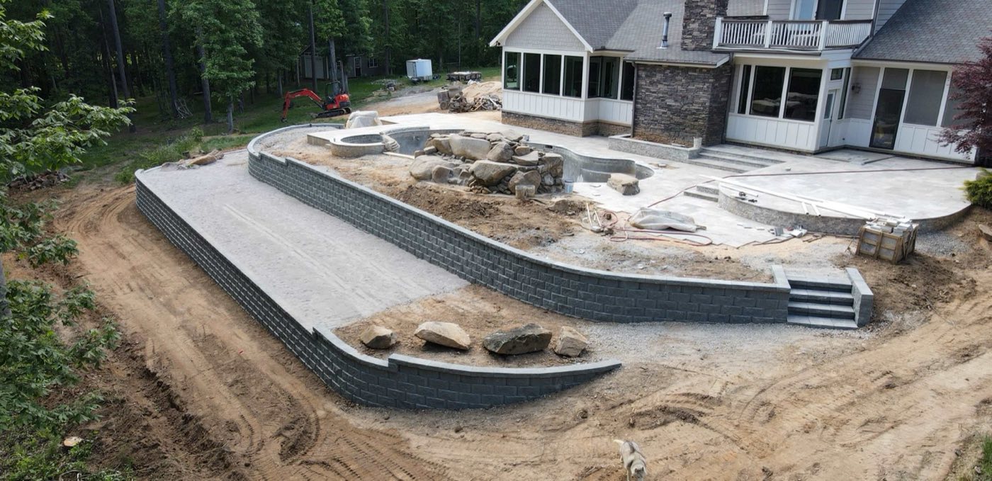 Long curved block retaining wall with built-in steps terracing a sloped Concord backyard