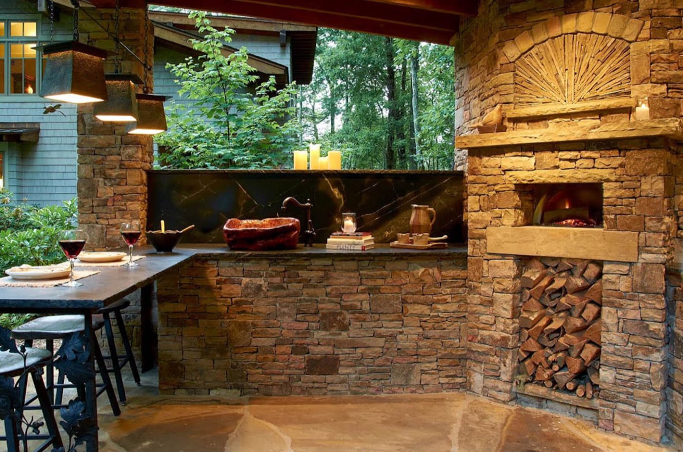 Stone outdoor kitchen with a wood-fired pizza oven, log store and bar seating under a covered roof