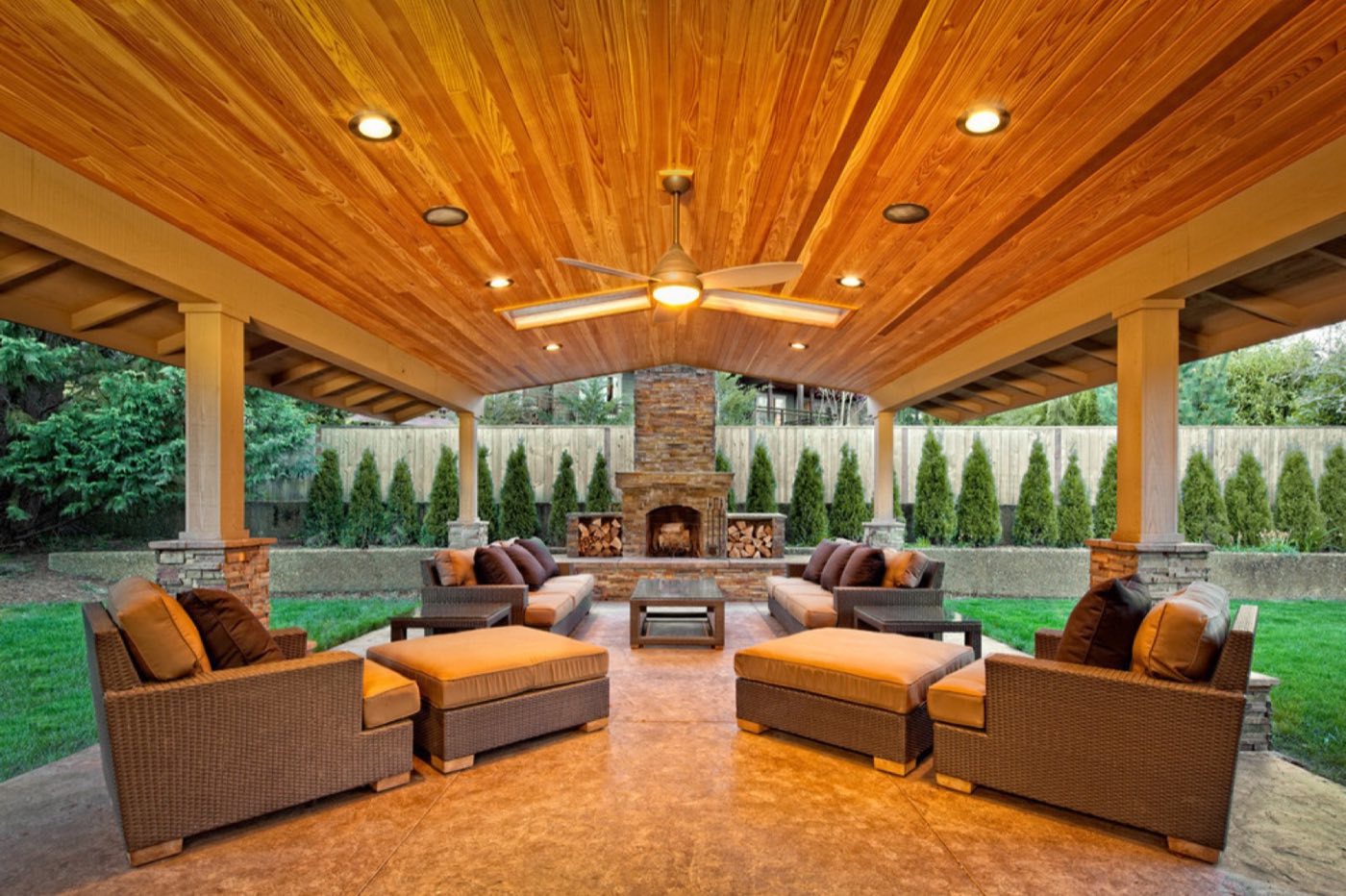Covered patio with a cedar cathedral ceiling, ceiling fan and a stone fireplace at the far end