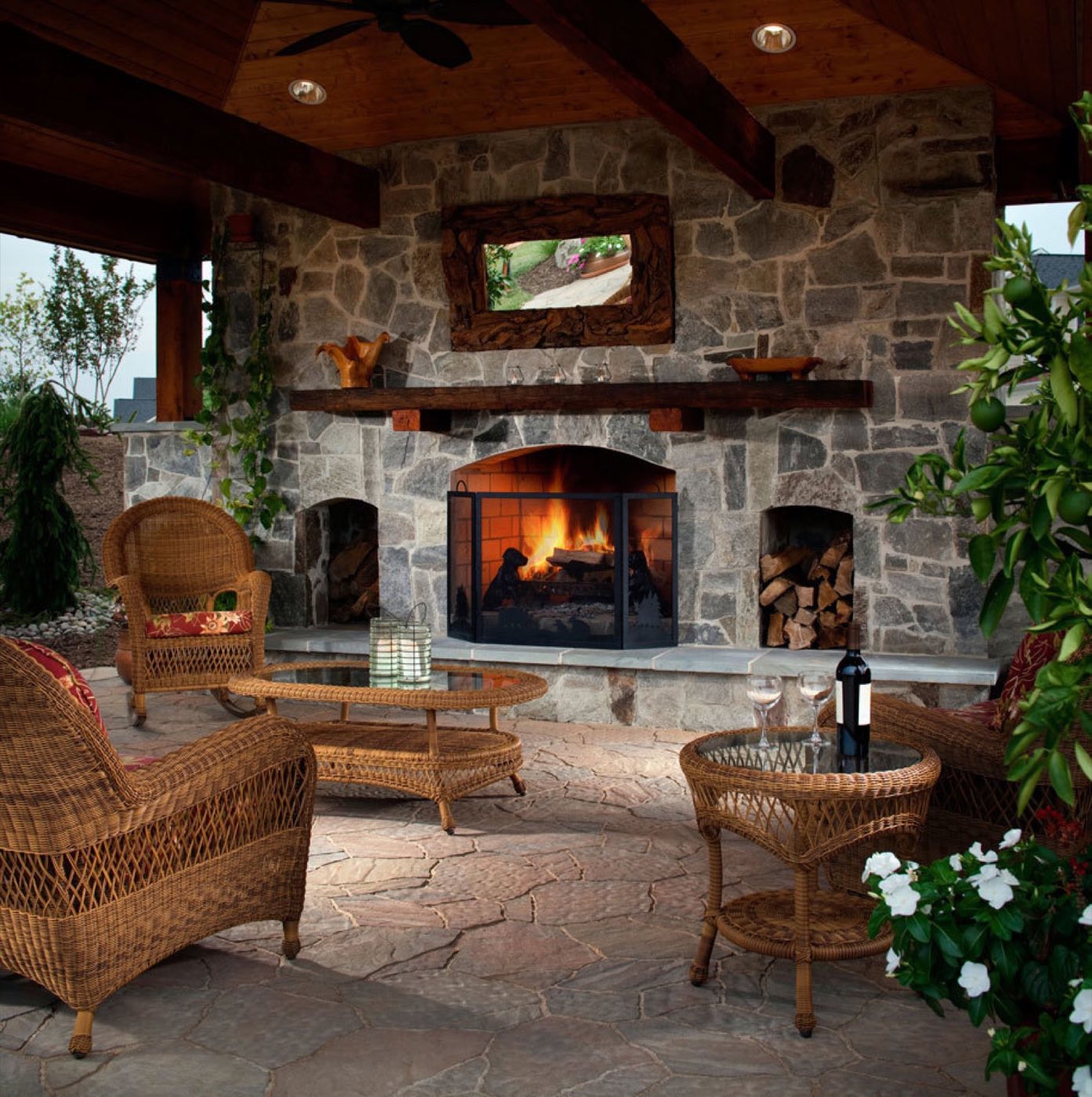 Stone outdoor fireplace with flanking log niches and a mounted TV beneath a beamed roof