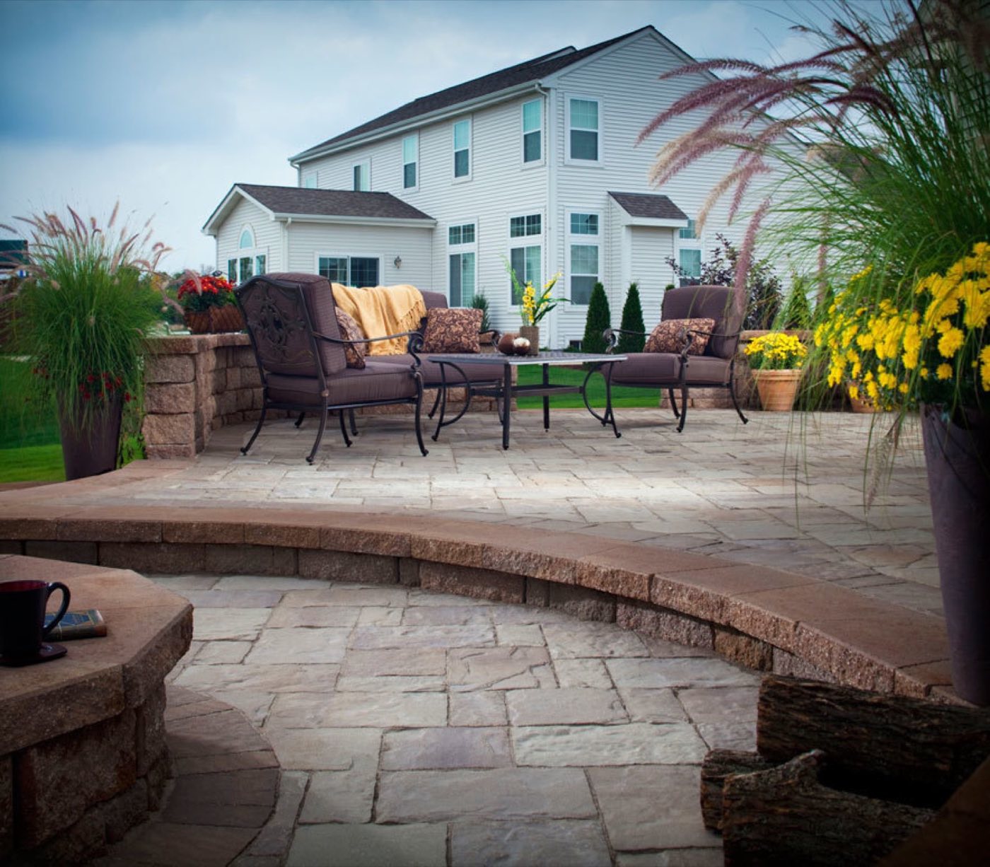 Raised paver patio edged with a block seat wall and planters behind a two-storey home