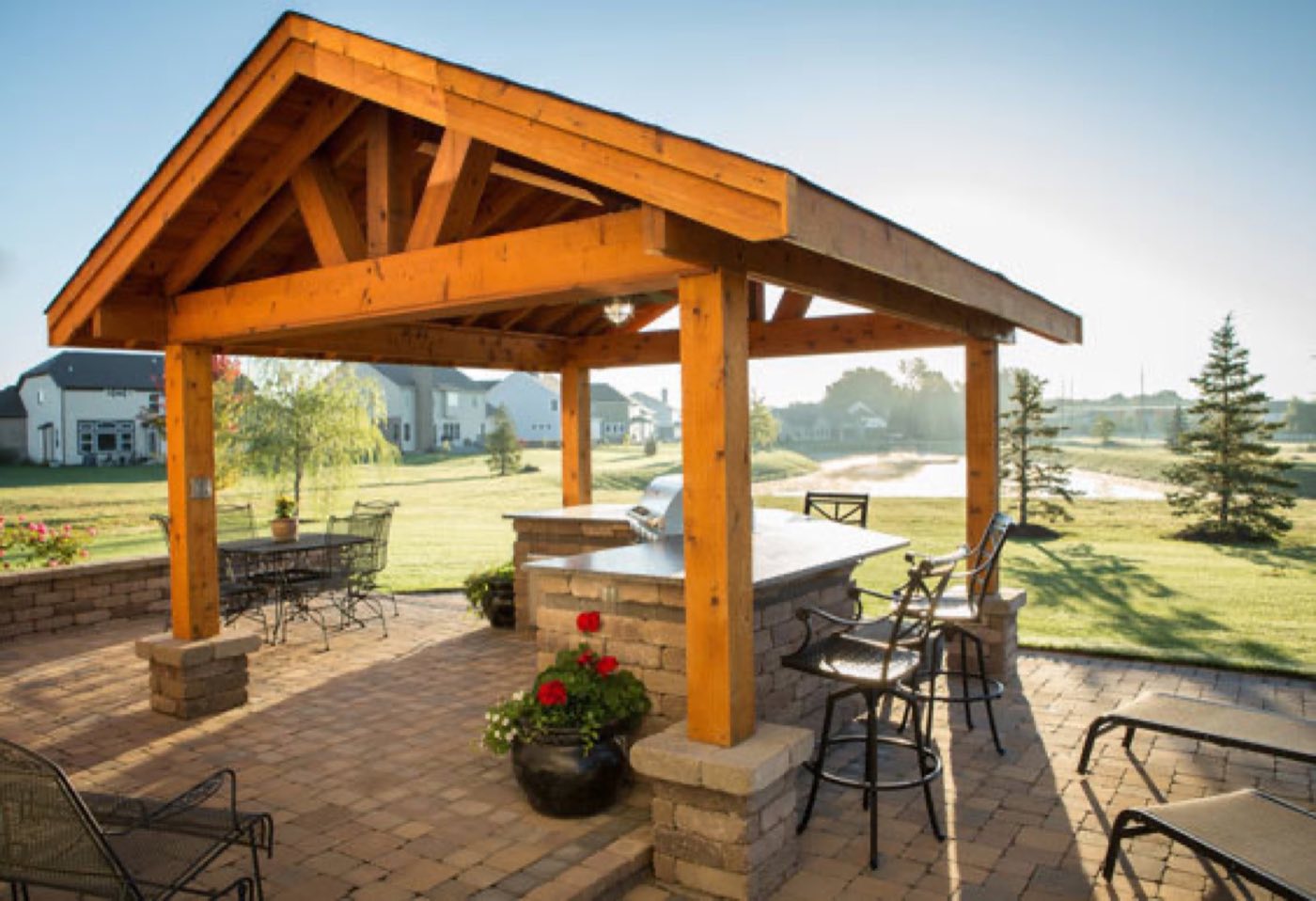 Gable-roof timber pavilion sheltering a stone-based outdoor kitchen bar on a paver patio
