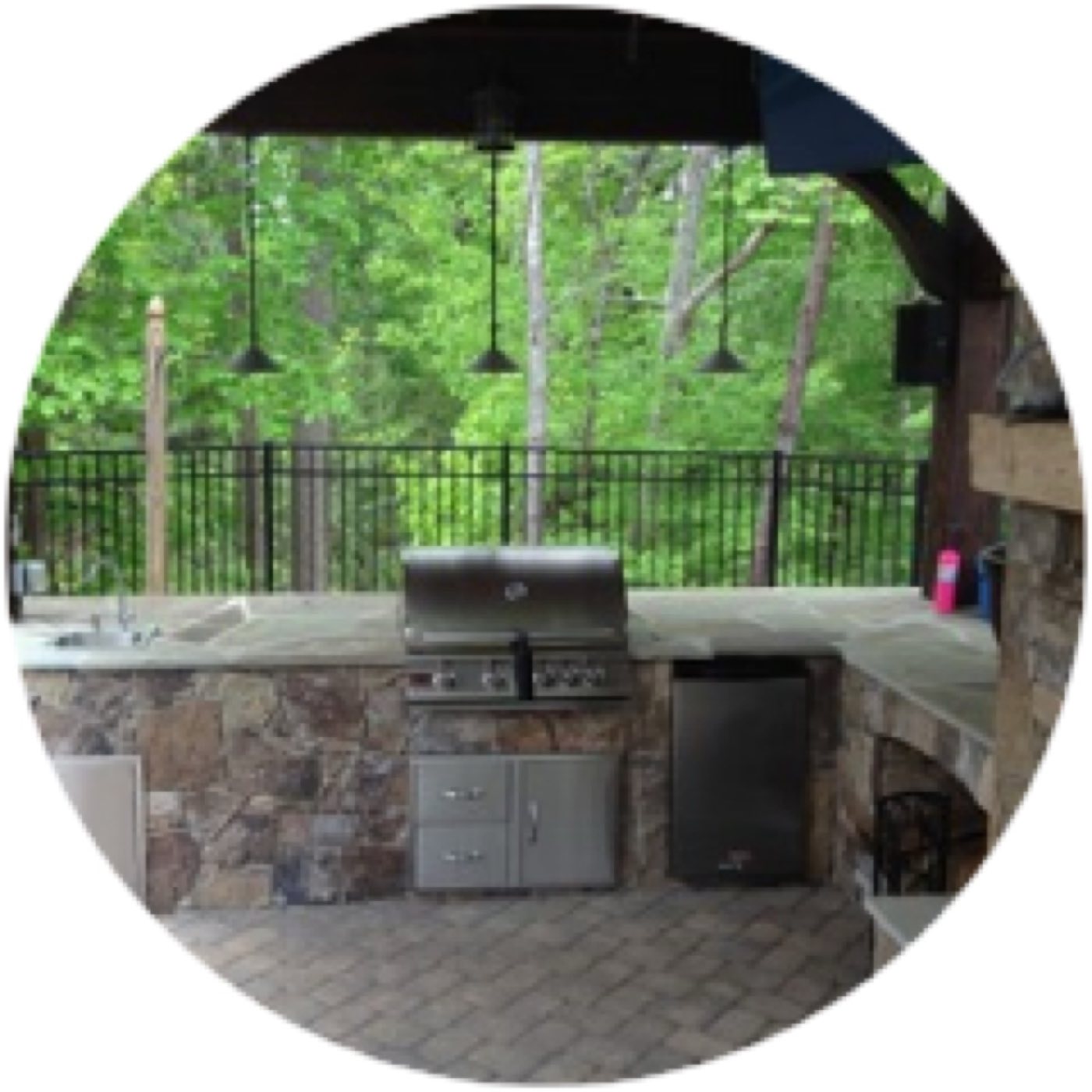 Covered outdoor kitchen with a stone-faced counter, built-in grill and pendant lights over a paver floor
