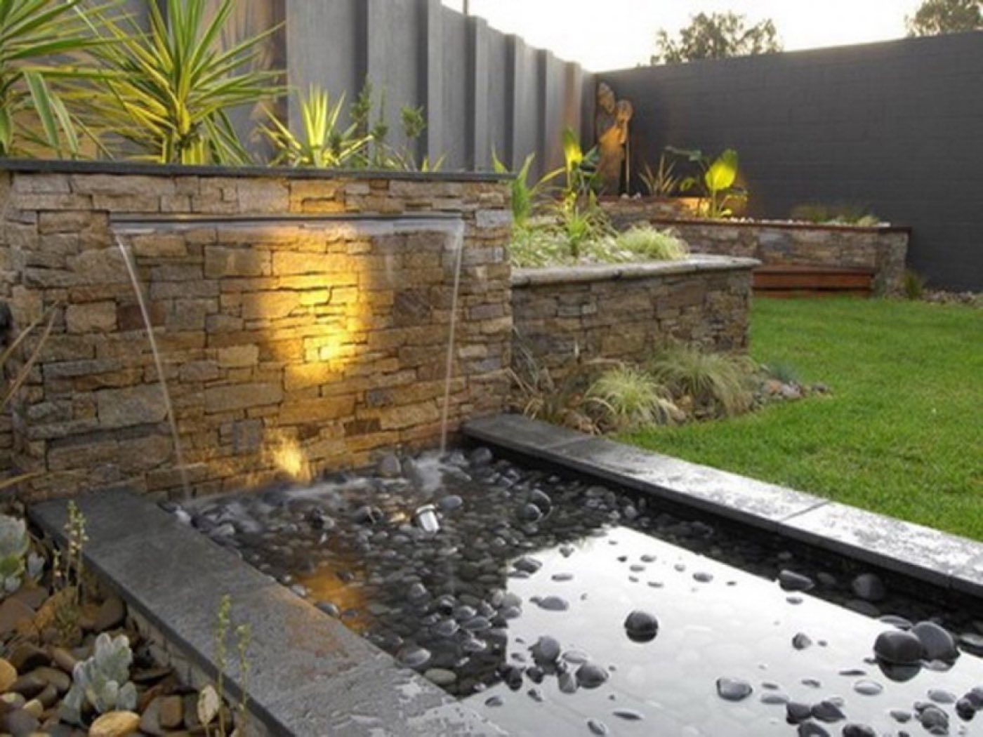 Stacked stone wall with twin sheer-descent spouts falling into a pebble-lined reflecting basin