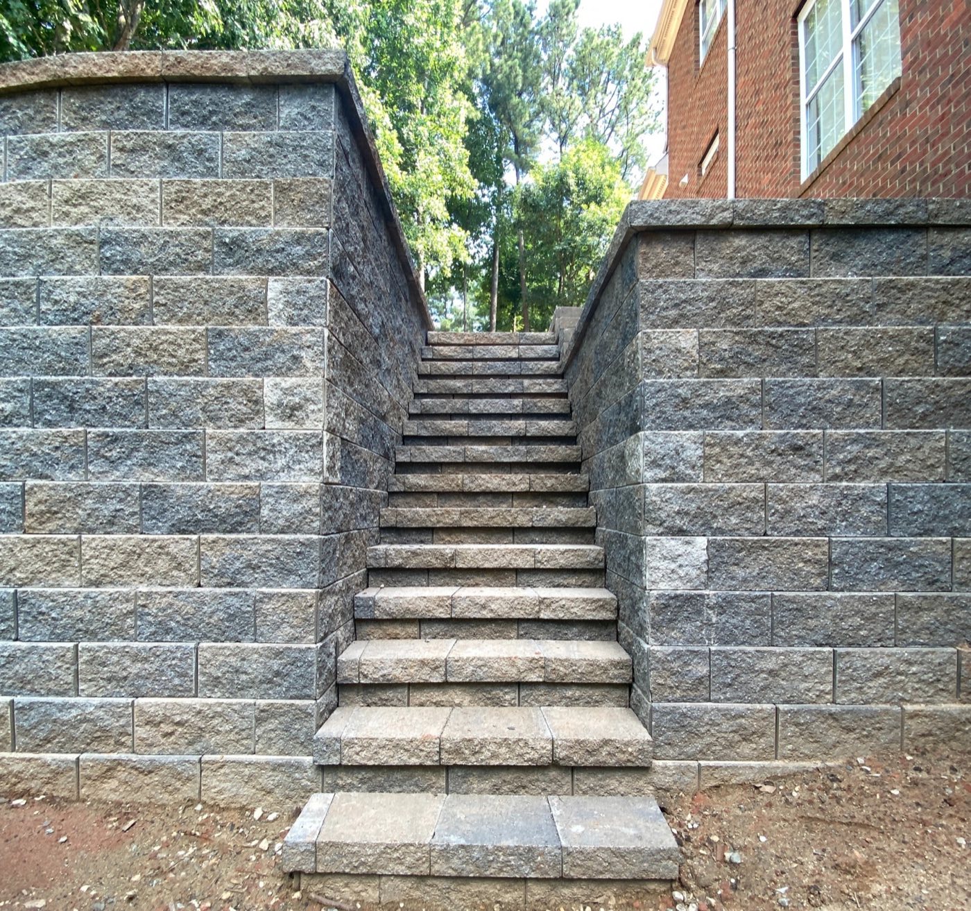 Block retaining wall flanking a flight of steps that climbs to a brick home