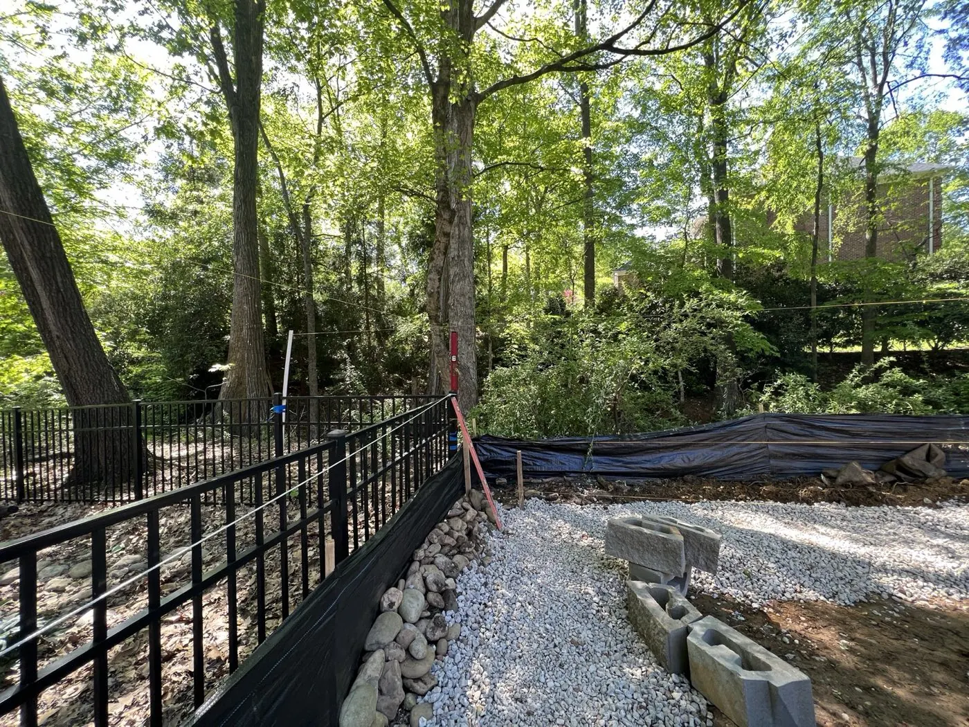 River rock drainage swale and silt fencing along a fence line, with wall block staged nearby