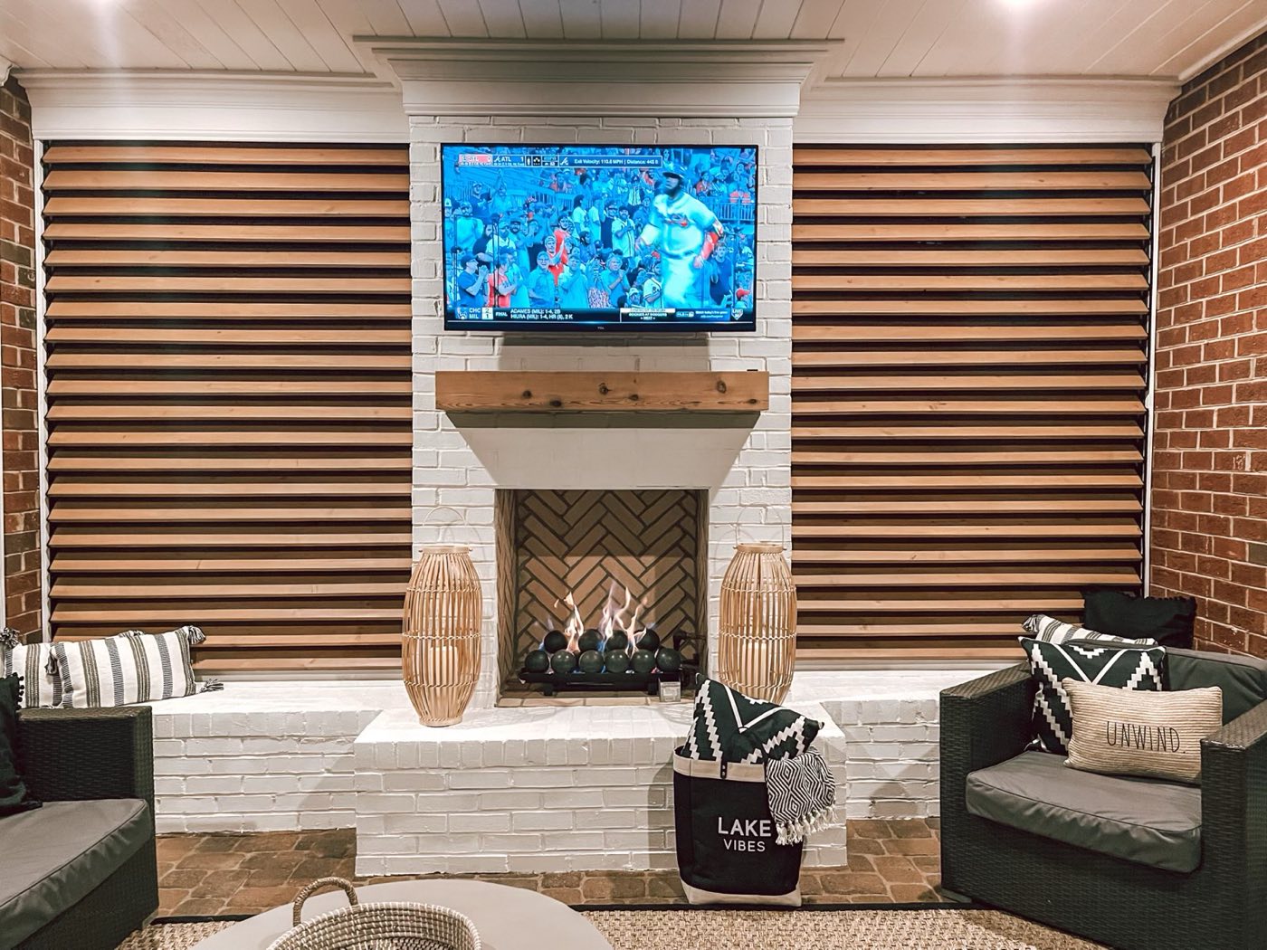 Painted brick outdoor fireplace with a herringbone firebox and mounted TV on a covered porch