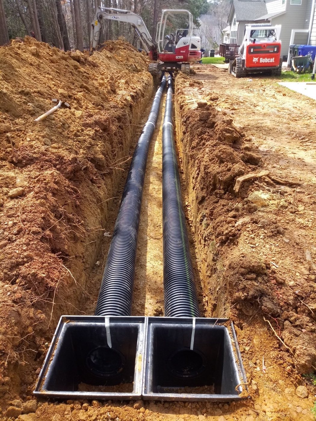 Twin corrugated drain lines bedded in an open trench running to a double catch basin