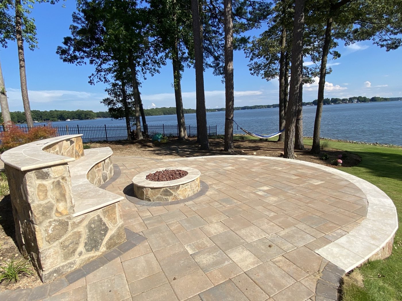 Curved paver patio with a stone seat wall and fire pit on the shore of Lake Norman