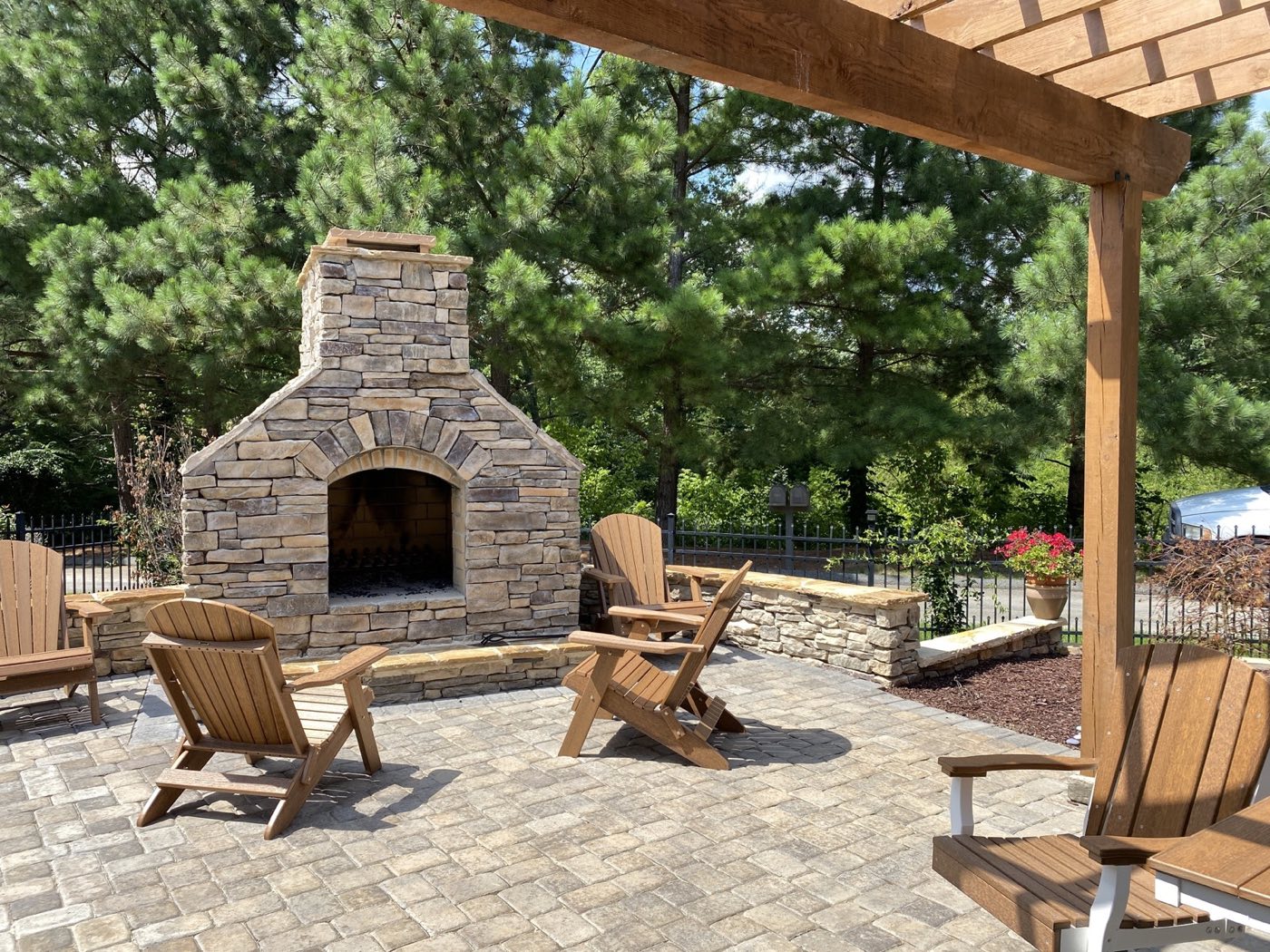 Stacked stone outdoor fireplace with an arched firebox on a paver patio ringed by Adirondack chairs