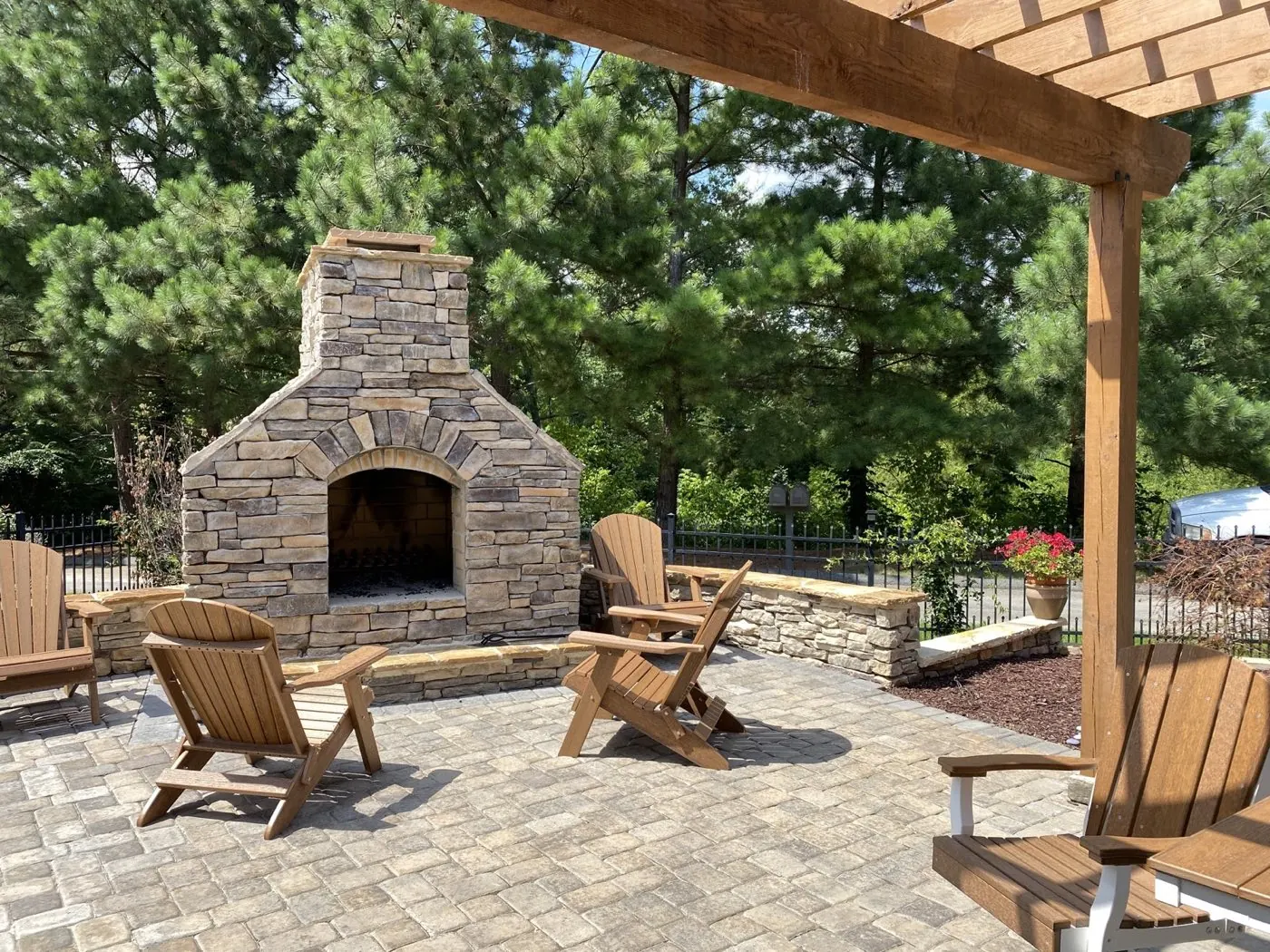 Stacked stone outdoor fireplace with an arched firebox on a paver patio ringed by Adirondack chairs