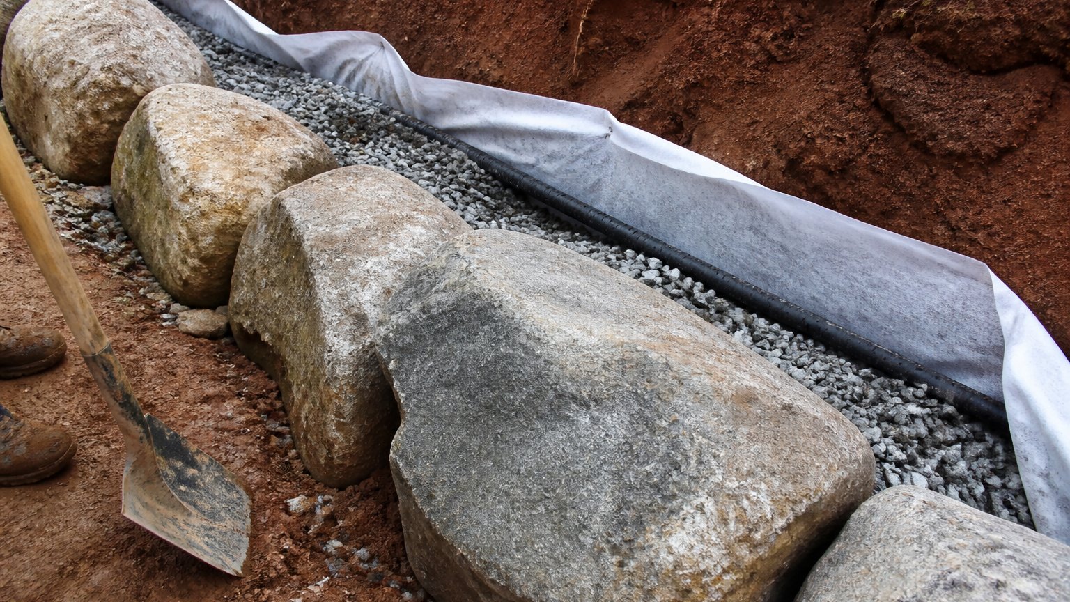 Boulder base course with filter fabric, crushed stone and black drain pipe behind it