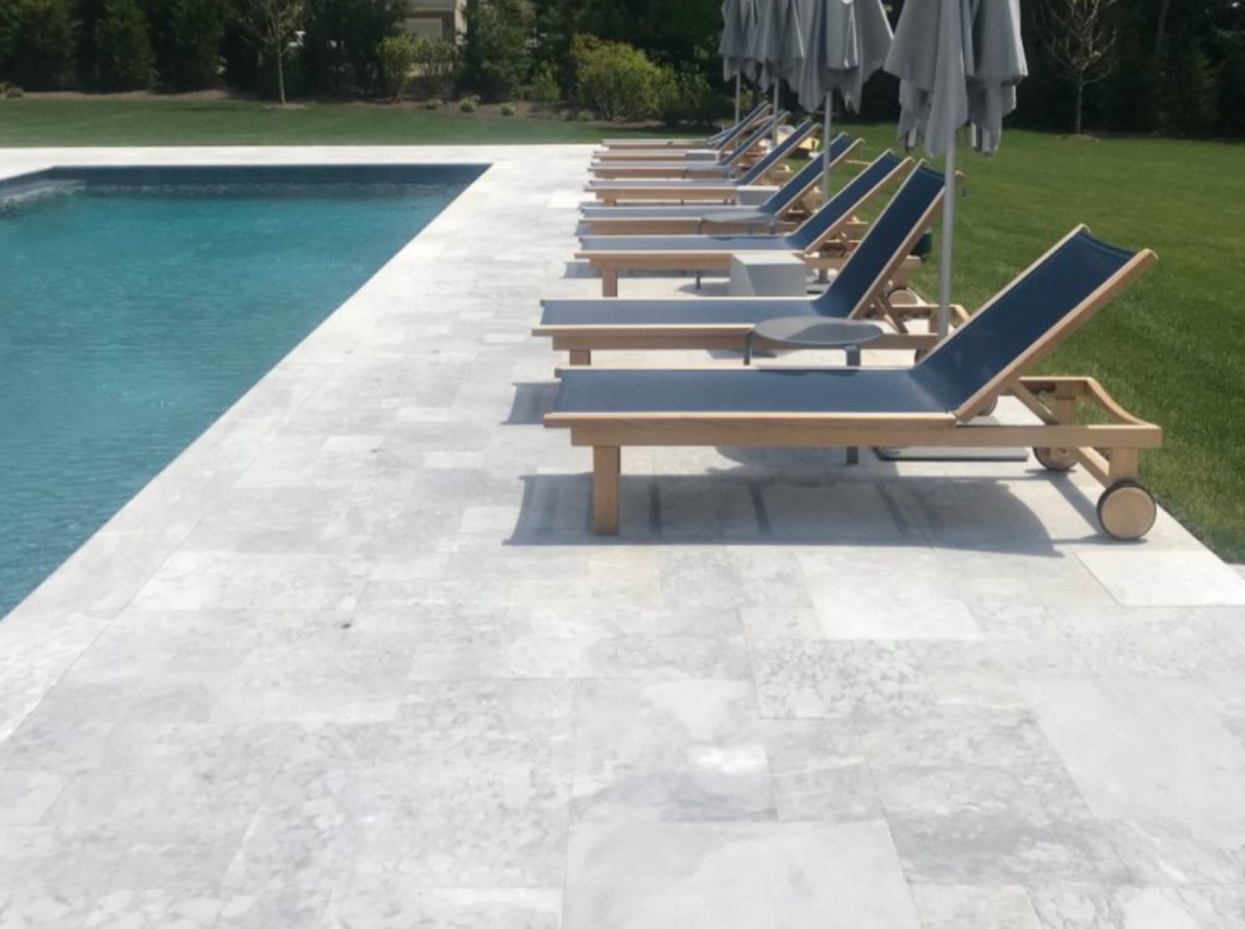 Silver marble pavers forming a pool deck lined with teak loungers
