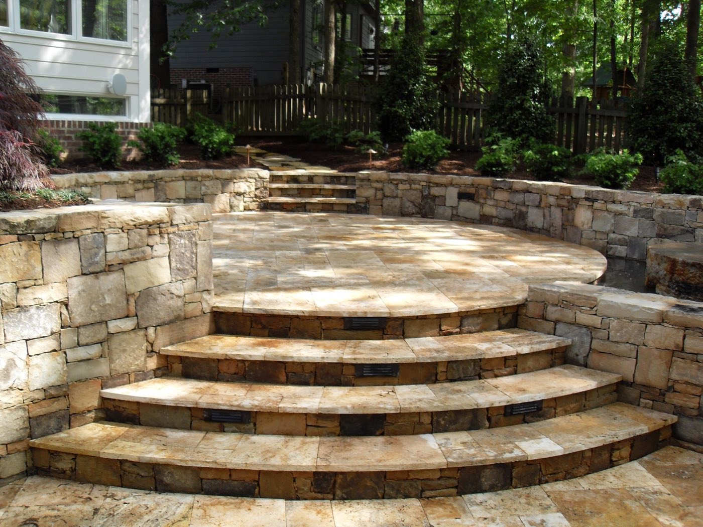 Curved stone steps with lit risers climbing between stacked stone walls to a raised patio