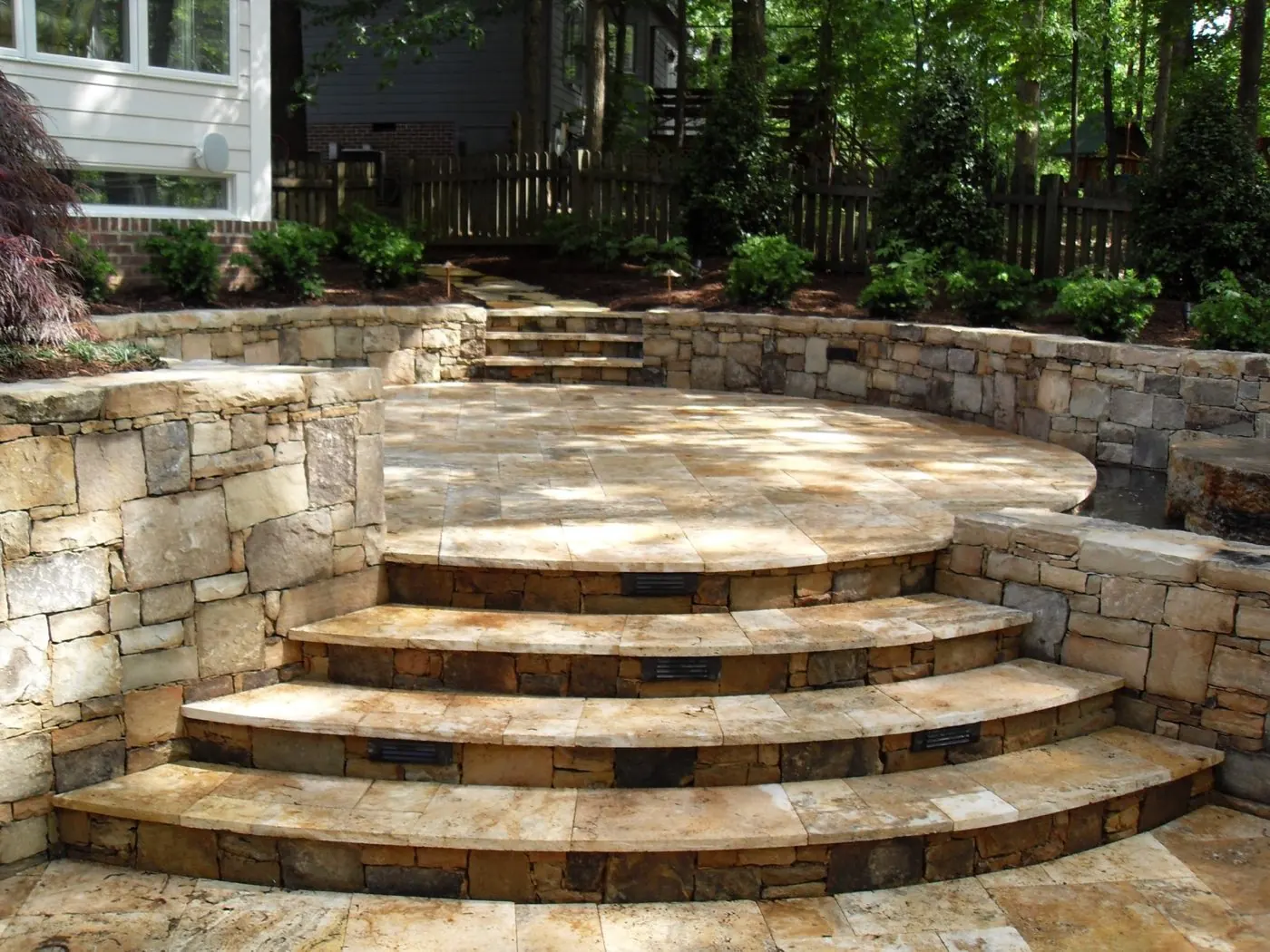 Curved stone steps with lit risers climbing between stacked stone walls to a raised patio